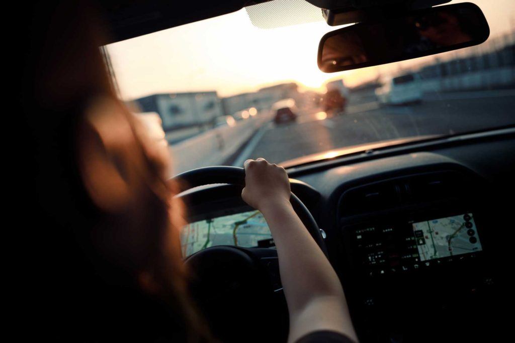 over the shoulder view of woman driving on highway at sunset