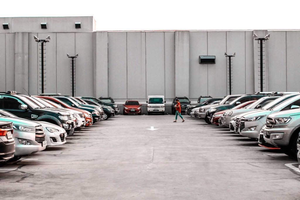 person walking through full parking lot of cars