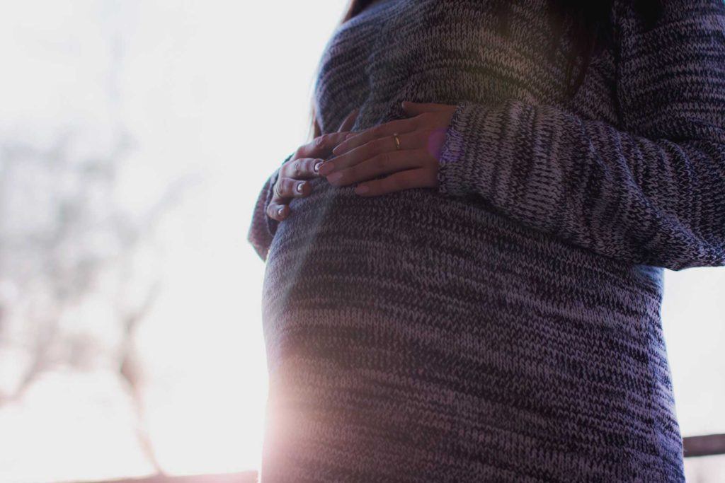 pregnant woman wearing sweater with hands placed over stomach