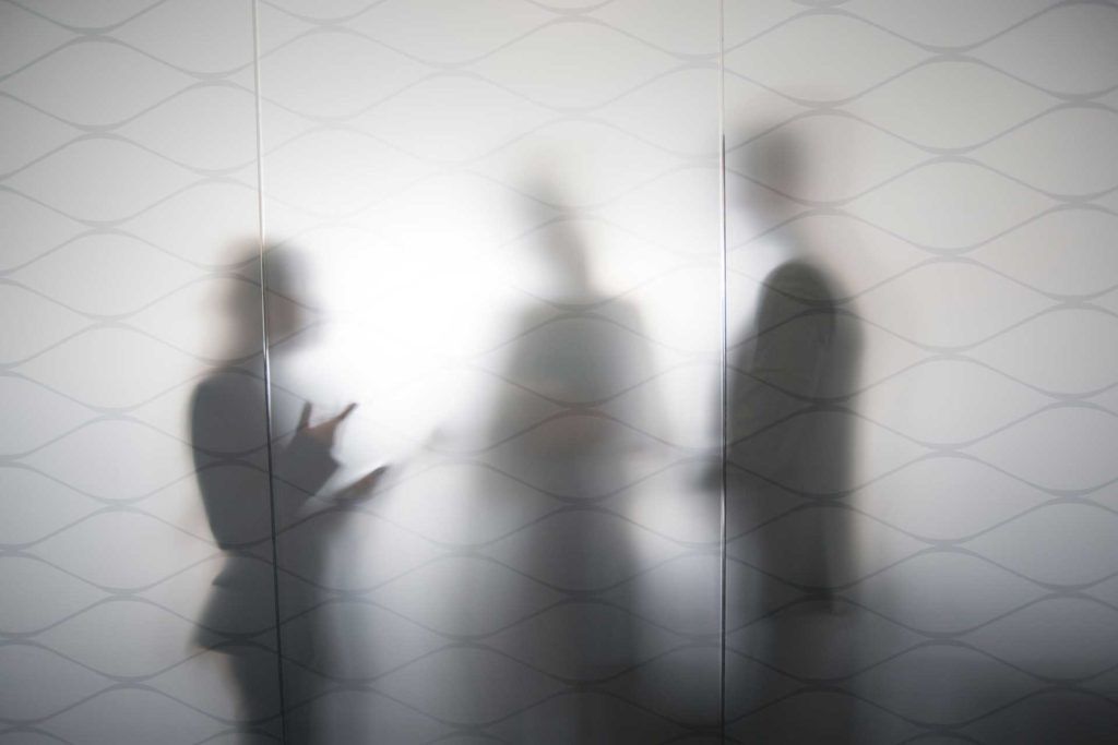 three silhouettes standing behind frosted glass